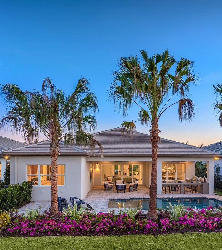 Florida home with a pool and lit lanai at dusk, framed by palm trees